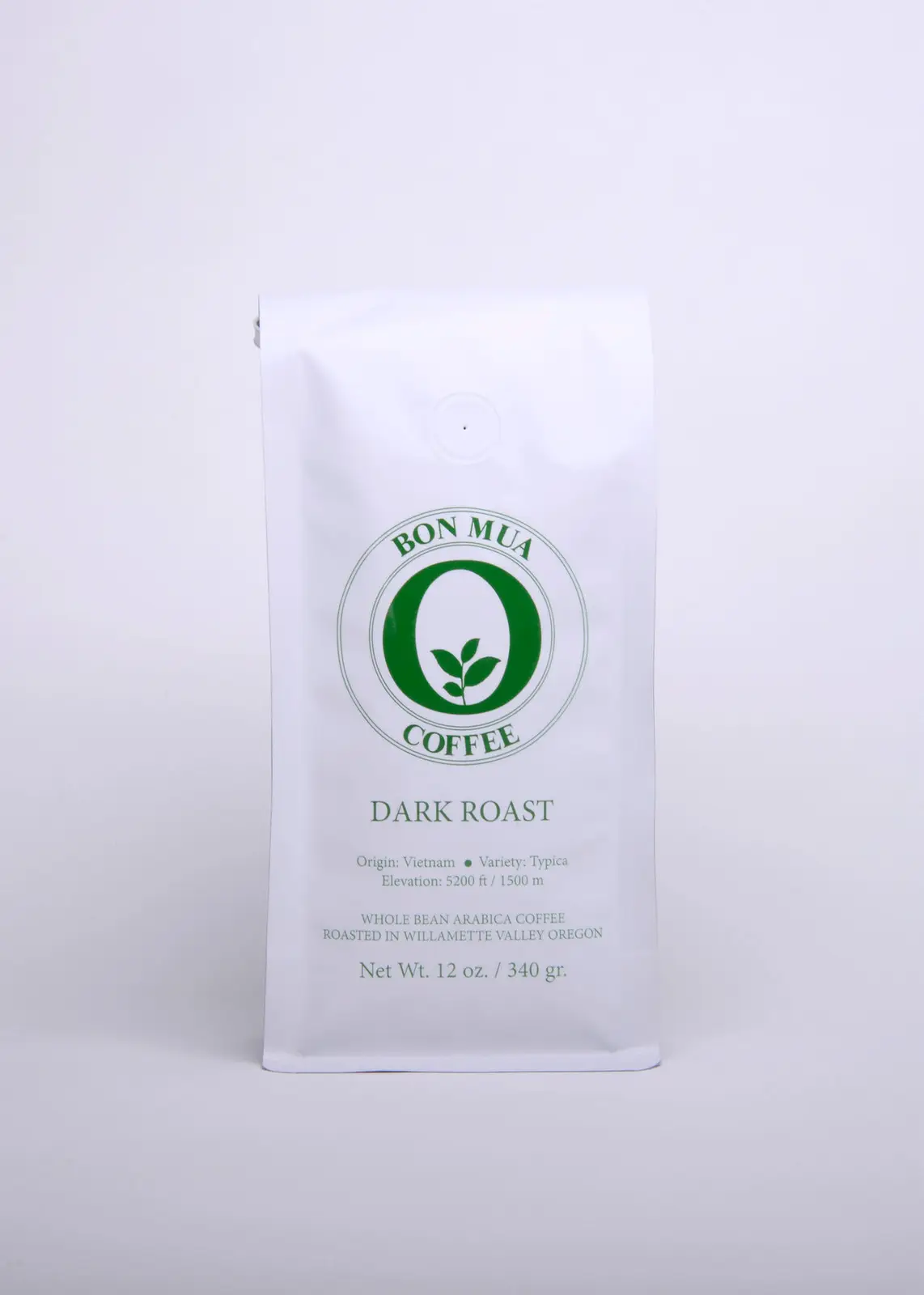 A single white Bon Mua Dark Roast coffee bag with a green O-shaped logo, photographed straight on against a pale grey background.