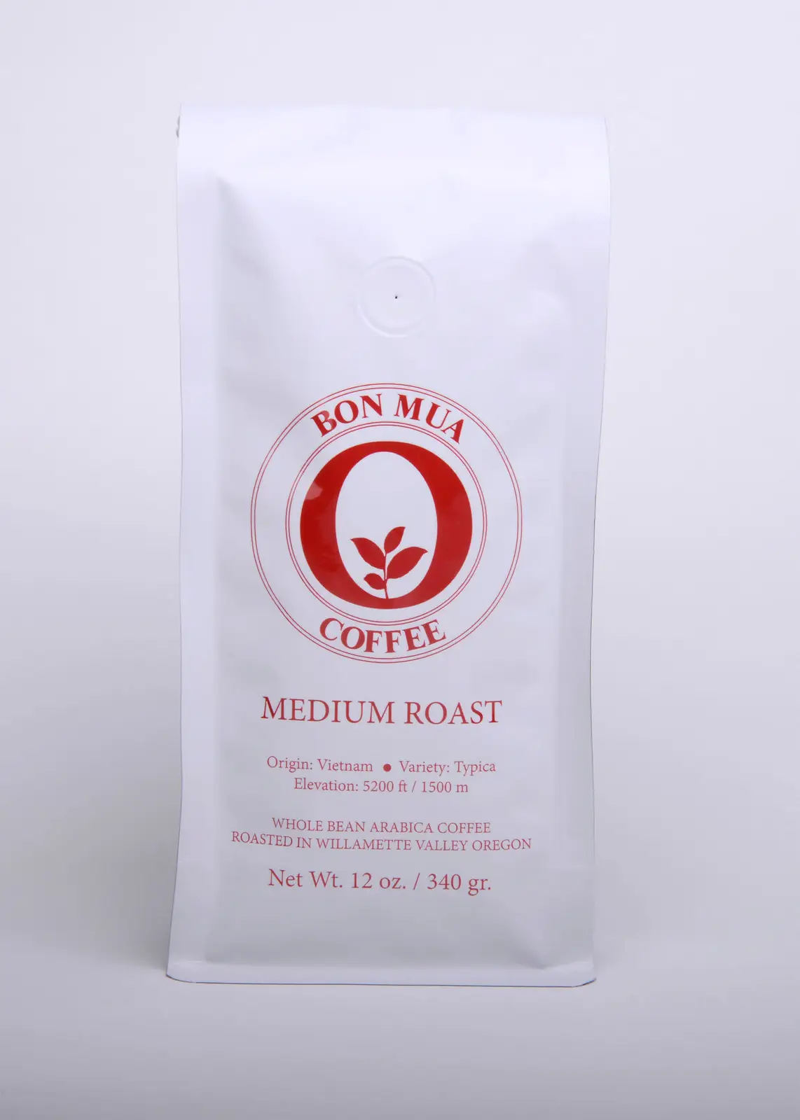 A single white Bon Mua Medium Roast coffee bag with a red O-shaped logo, photographed straight on against a pale grey background.