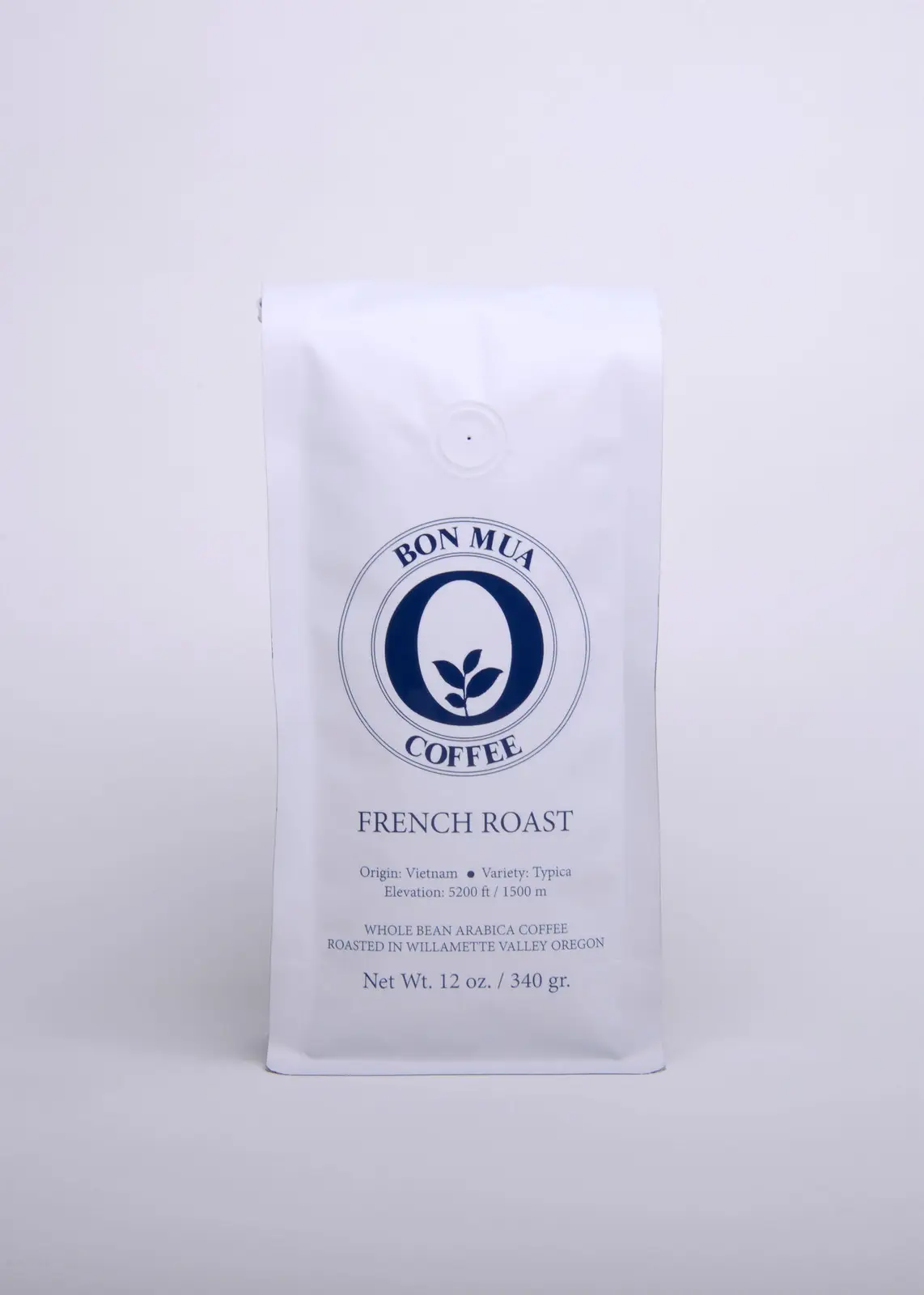 A single white Bon Mua French Roast coffee bag with a navy-blue O-shaped logo, photographed straight on against a pale grey background.