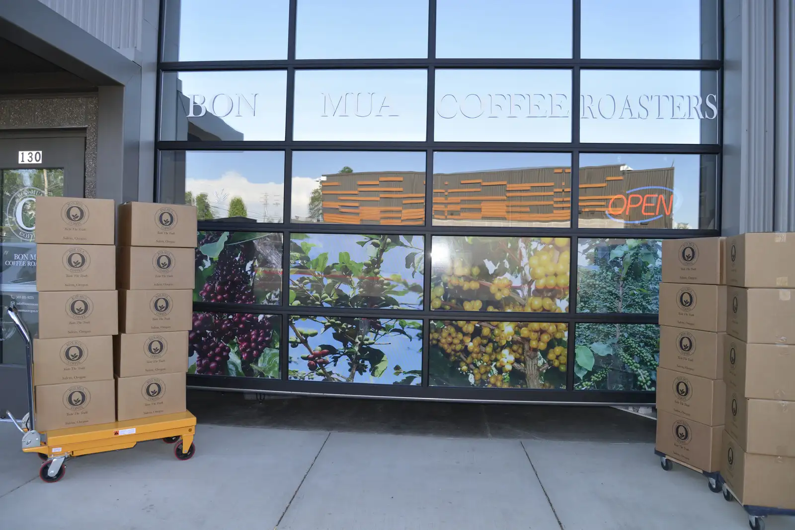 The Bon Mua Coffee Roasters storefront in Salem: a glass garage-door front etched with the company name over a coffee-cherry mural, with an OPEN neon sign in the window.