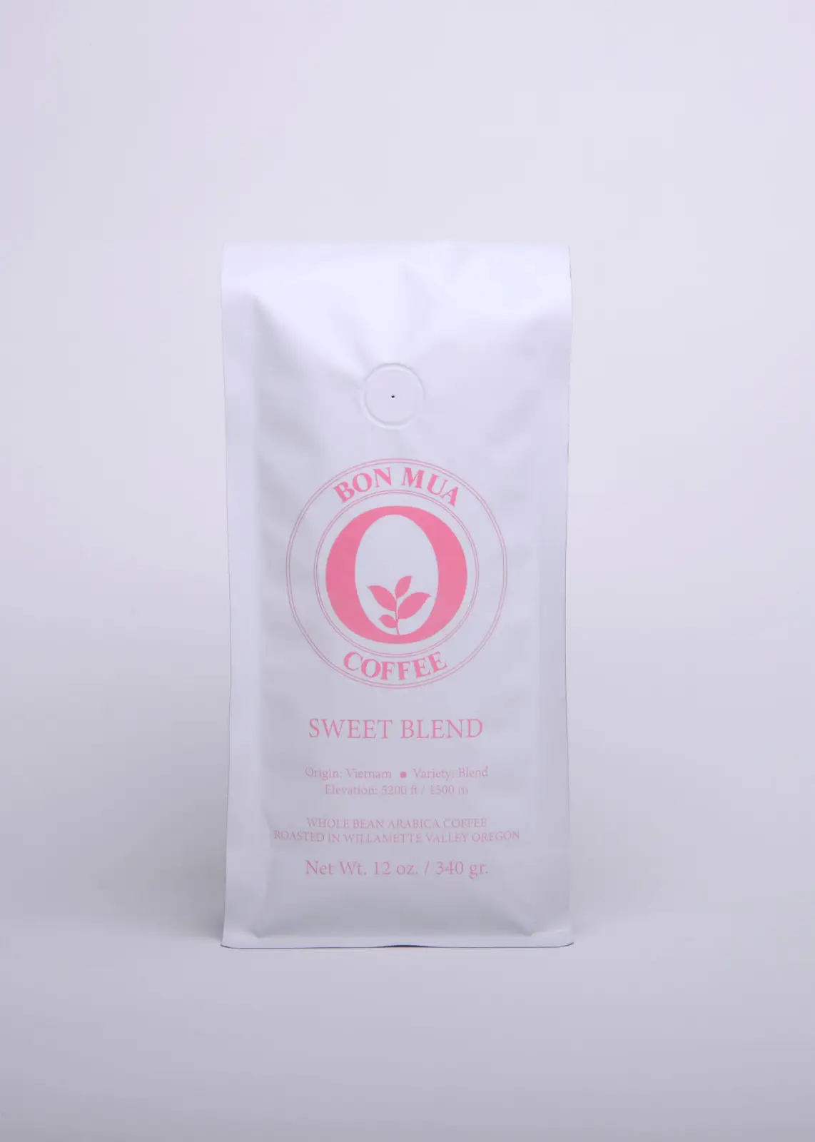 A single white Bon Mua Sweet Blend coffee bag with a pink O-shaped logo, photographed straight on against a pale grey background.